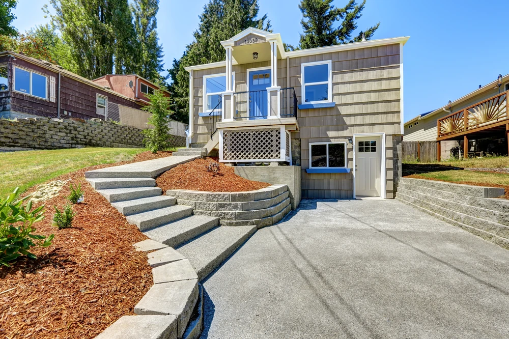 Fresh concrete patio and tiered retaining walls create a clean entry walkway for a blue door home.