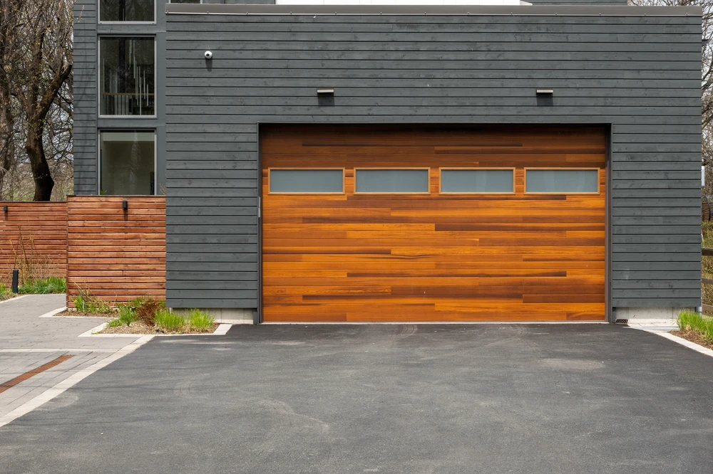 Curved blacktop driveway leading to a large stone and siding home with two white garage doors and landscaped lawn.