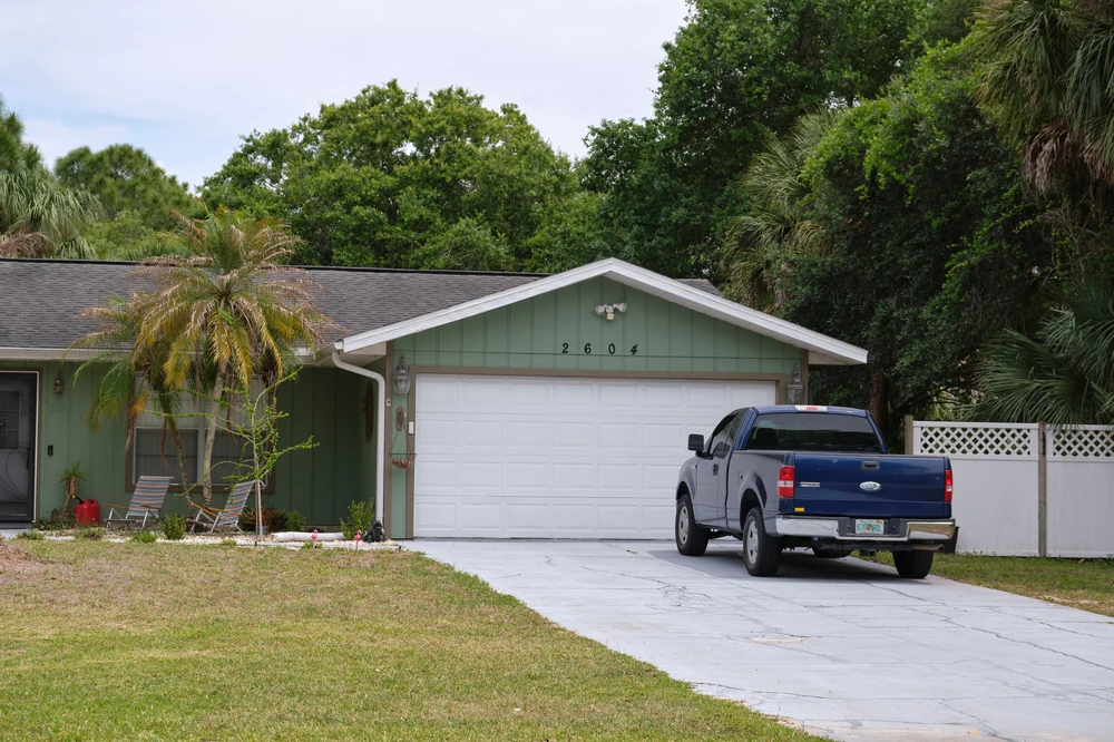 Blue pickup parked on a white concrete driveway in front of a pale green home with a white garage door.