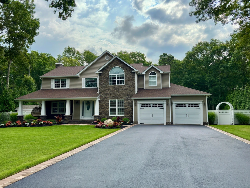 Modern wood garage door beside a black asphalt driveway on a gray contemporary home with horizontal siding.